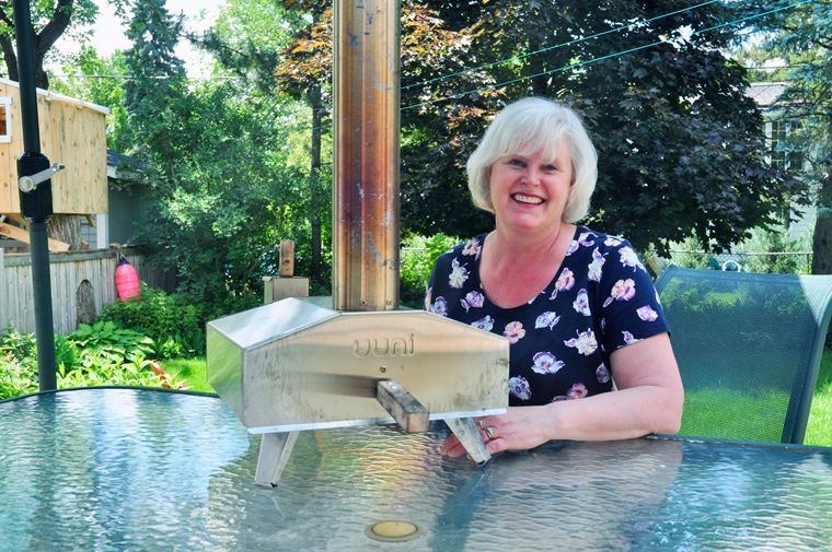 Like many people, food writer Paula Roy’s love affair with pizza dates back to her childhood. Her taste buds have matured since then! She’s pictured here with her portable backyard pizza oven. Photo by Andrea Tomkins