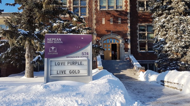 The exterior of Nepean High School. The purple and white entry sign is on top of a snow covered lawn with the red brick building in the background.