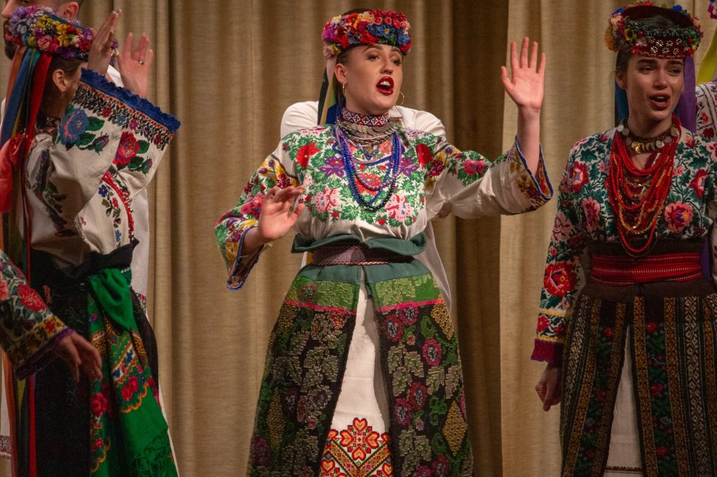 A woman in a colourful dress moves her arms as she sings. 