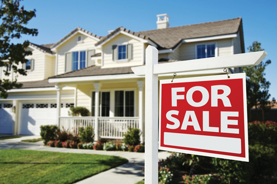 An Adobe stock image of a red "For Sale" sign in front of a two storey white house