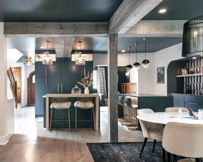 A professional photo of the inside of a renovated dining room and kitchen. There are metallic finishes and dark blue paint on the walls.||