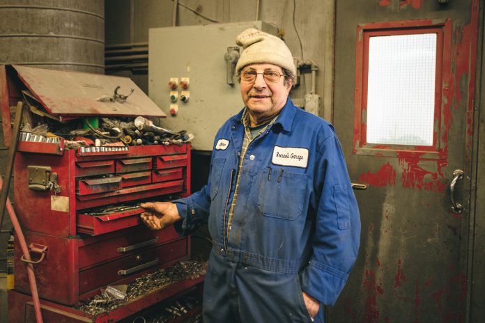 A man stands in a mechanic's uniform next to a red toolkit|A man stands in a mechanic's uniform next to a red toolkit with cars and mechanics behind him|A hand reaches into a tool chest and picks up a wrench|A man stands outside of Romeo's Garage & Body Shop's front garage door in the snow