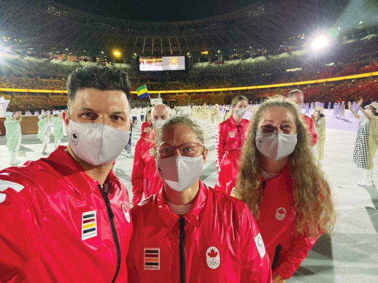 A group of three Olympians wearing Team Canada jackets stand in a large arena in Tokyo|