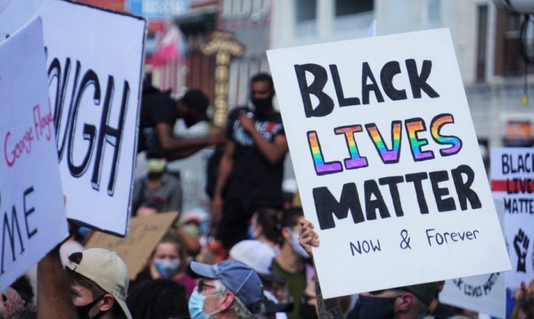 A white posterboard with the text "Black Lives Matter" written in black and rainbow lettering