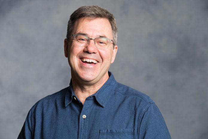 A professional headshot of Eric Coates against a grey background