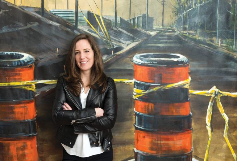 Eryn O'Neil stands with her arms crossed against one of her LRT artworks