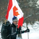 A man dressed for a cross-country skiing outing has a large Canada flag hanging out of his backpack.