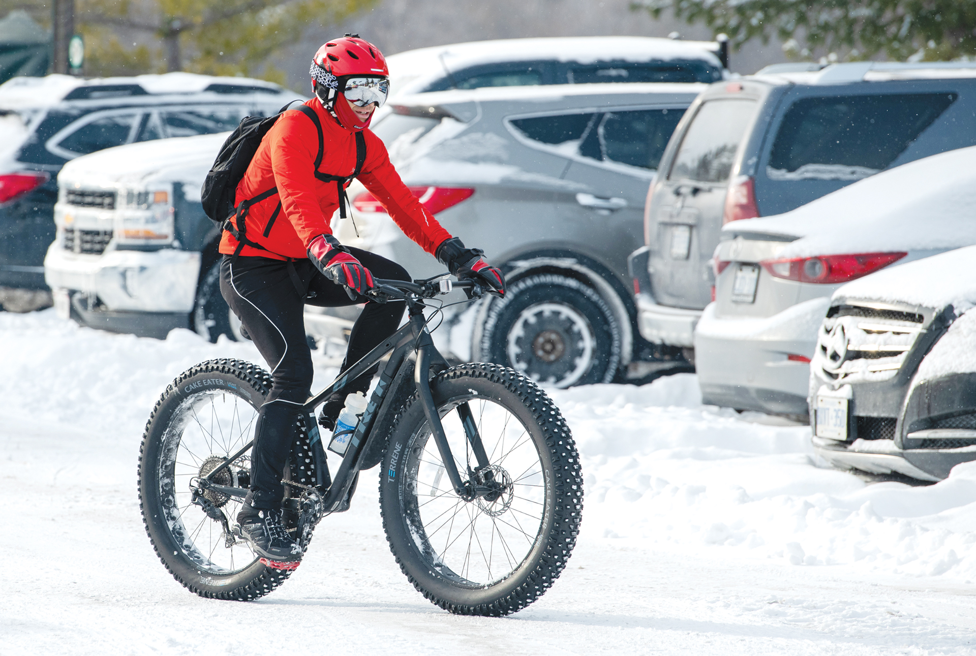 A person rides their fat bike in a snowy parking lot.