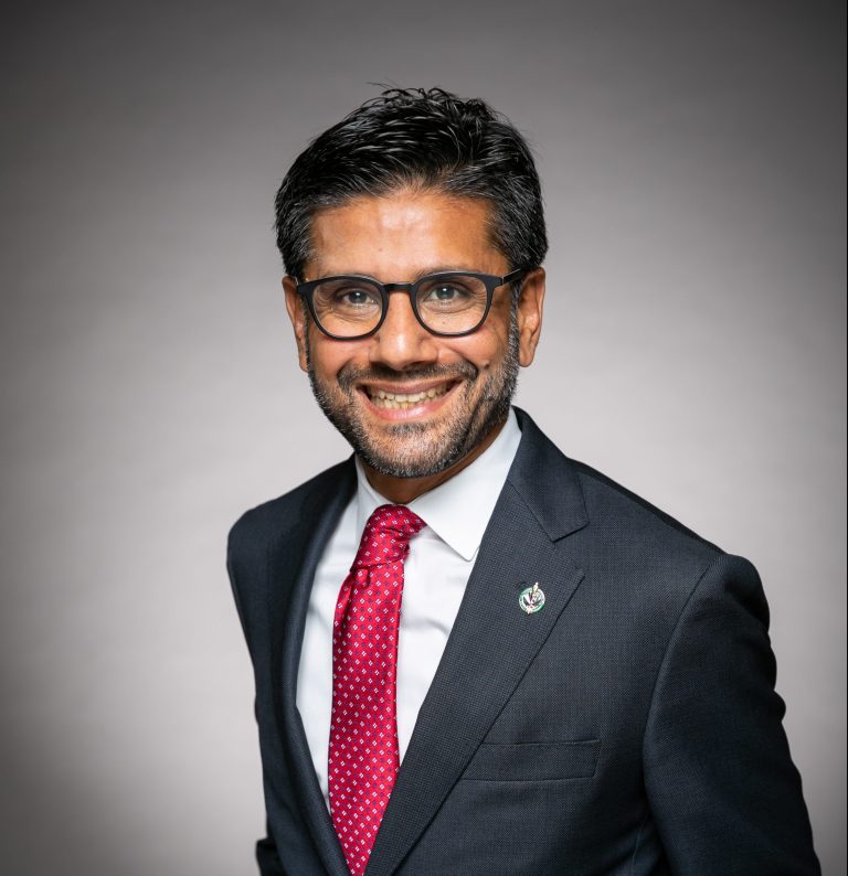 A professional photo of Yasir Naqvi against a gradiant grey and white background.