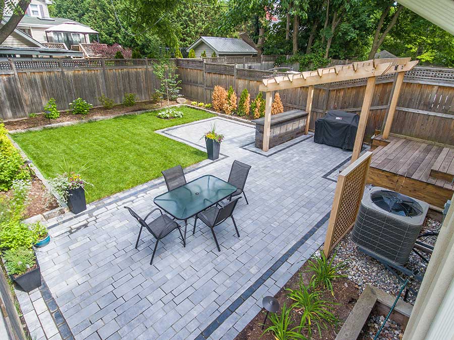 A backyard in Ottawa is seen with a table and chairs, manicured lawn and pergola.