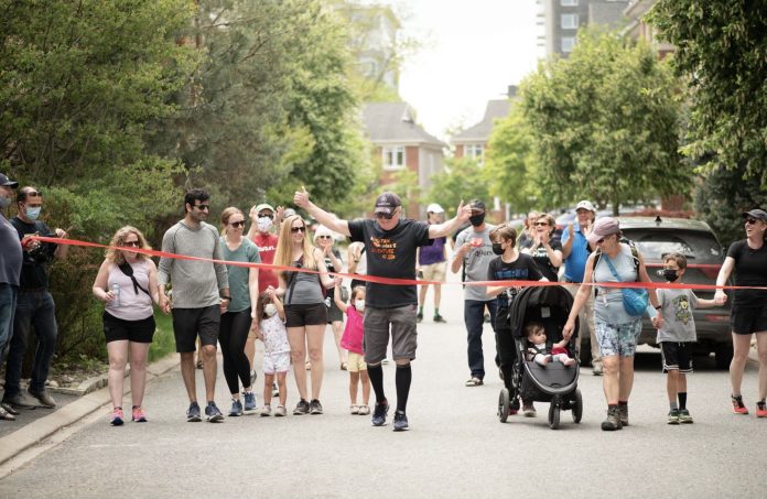 Michael Baine is seen with his family crossing the red ribbon finish line for his half-marathon walk in Westboro|Michael Baine is seen in a hospital bed wearing a blue mask and blue slippers|Michael Baine is seen walking outside with walking sticks