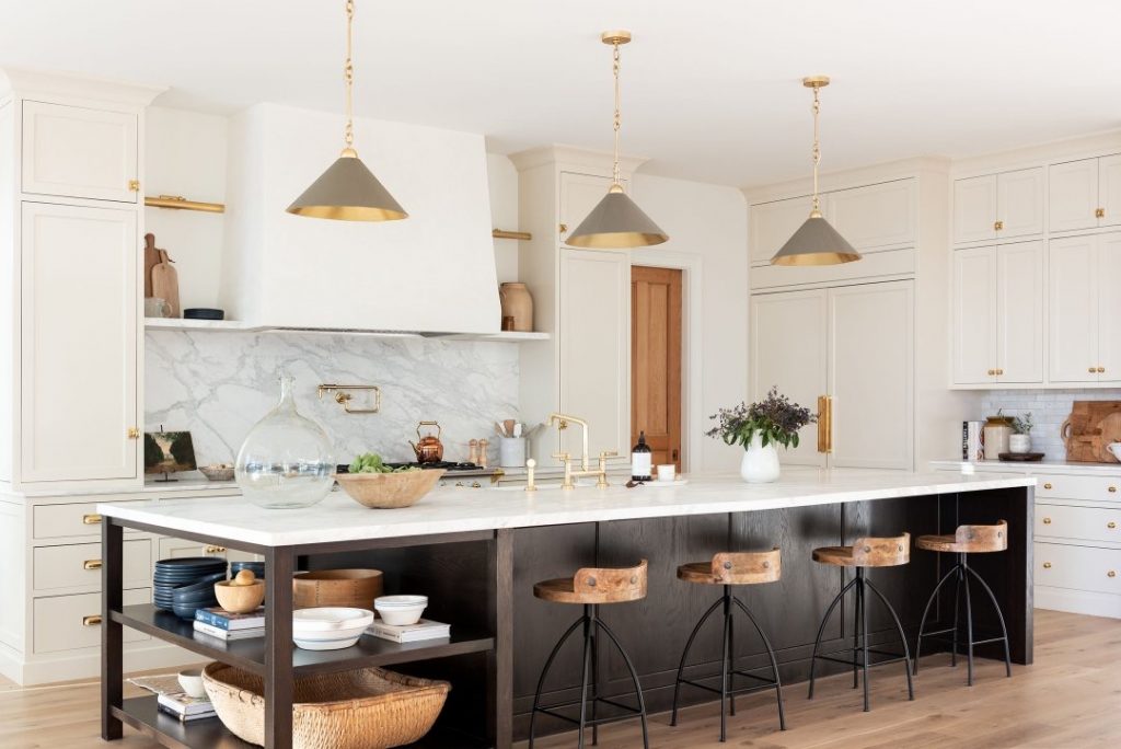 A renovated black and white kitchen with a long island and overhead gold and silver lights.||||