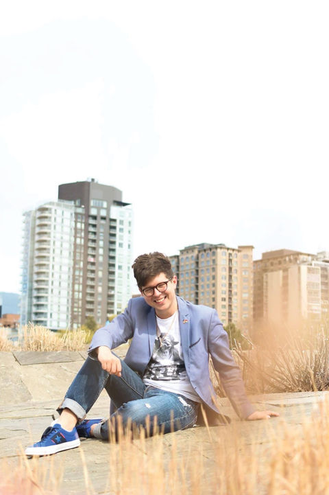 A man sits in an open field in front of buildings in Ottawa in a professional photo|