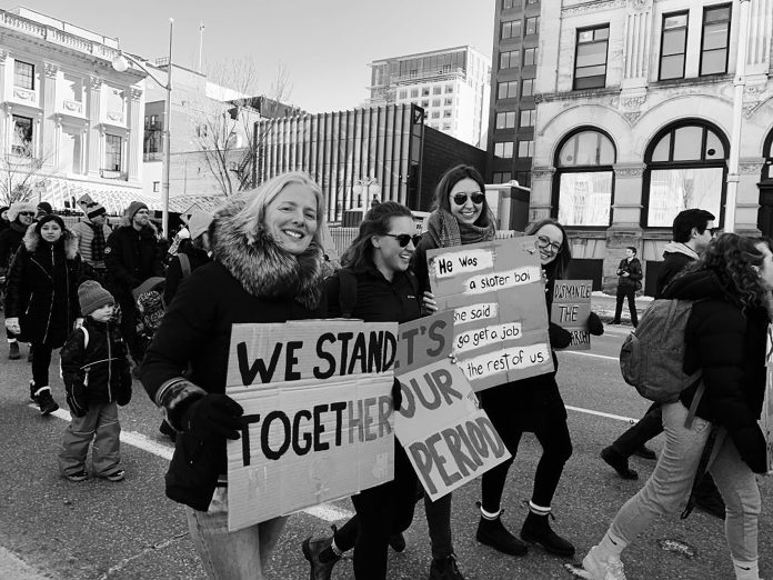 A black and white photo of MP Catherine McKenna walking in a Women's Day March in 2020 in downtown Ottawa.