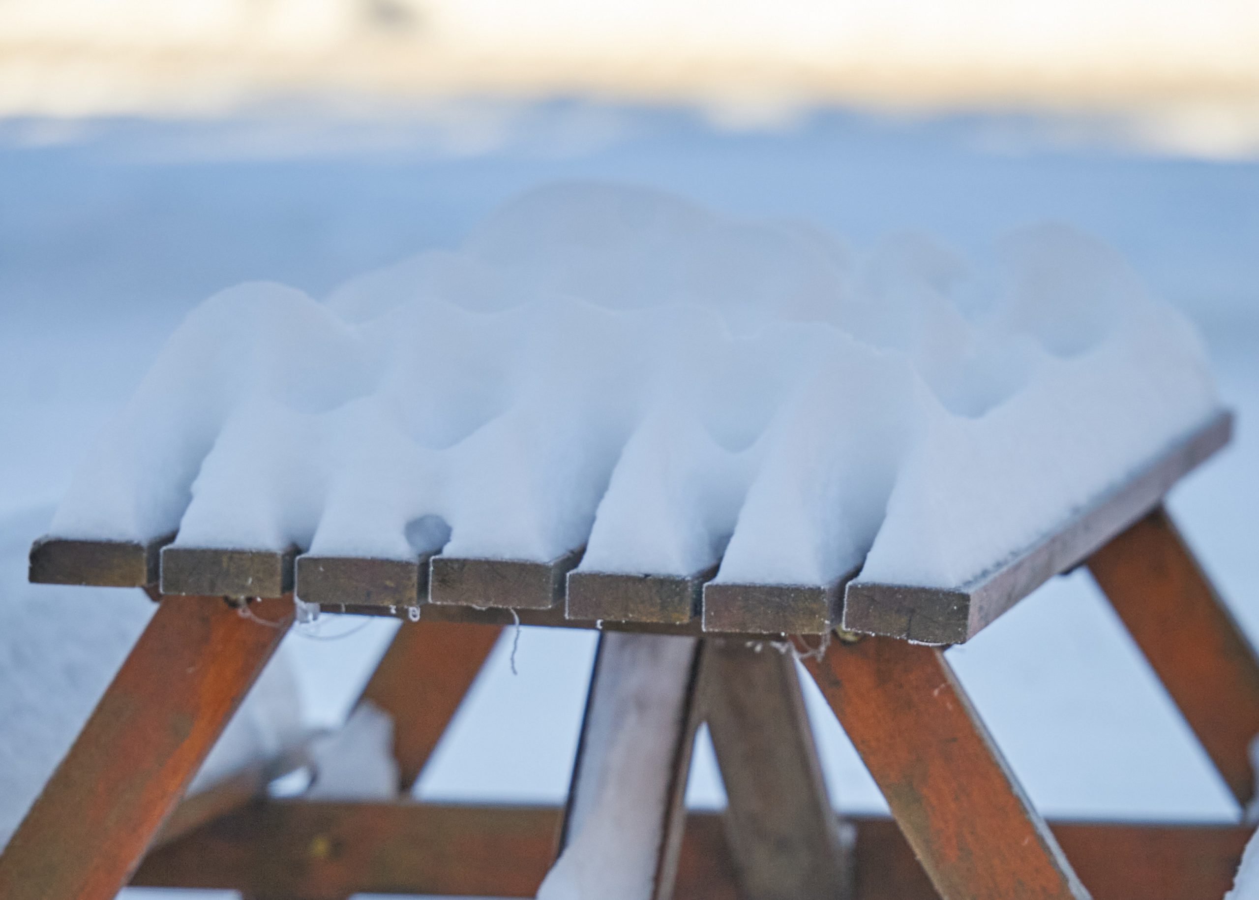 A wooden bench is covered in inches of fresh snow