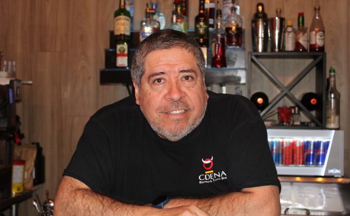 Marcelo Cadena sits at the bar of Cadena Restaurant. He is wearing a black tee shirt.