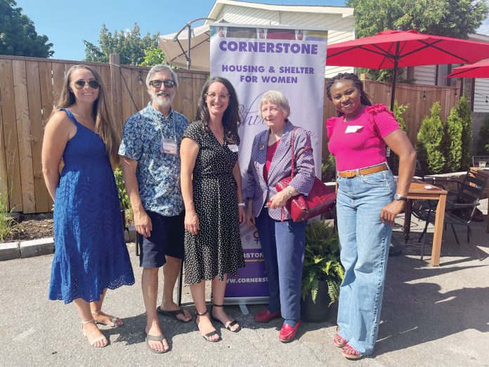 A group of four women and one man stand next to a purple banner for Cornerstone Housing for Women on a sunny day in Westboro.|A group of three women make art and crafts at a Cornerstone Housing for Women residence.