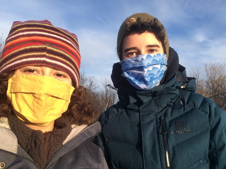 Two teenagers stand next to one another wearing masks on a sunny day in Ottawa