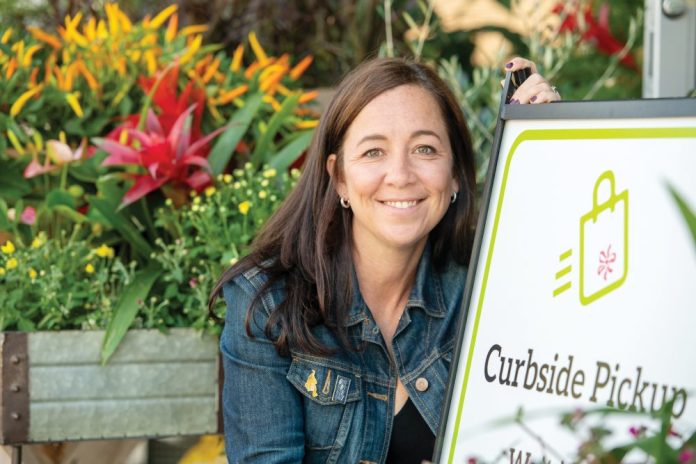 Elizabeth Young of Flowers Talk Tivoli poses with a curbside pickup sign outside her store.