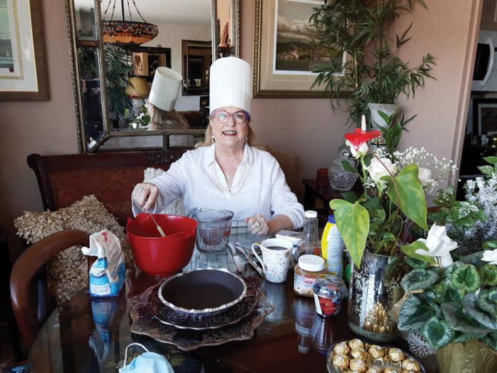 A woman wearing a chef hat is seen sitting behind a table with backing supplies and equipment in front of her|A headshot of Brian Harrison against the backdrop of a river on an overcast day