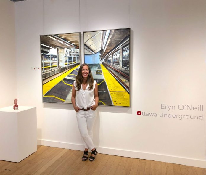 A photo of local Artist Eryn O’Neill standing in front of her newest body of work