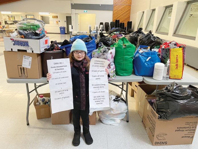 An 8-year-old girl stands in front of a table with donated items piled on top of it at the Tom Brown Arena Respite Centre|