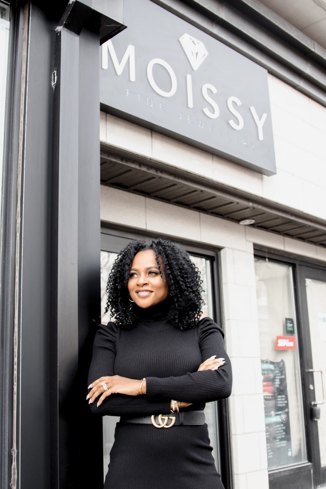 Colleen Montague stands outside of Westboro's Moissy Fine Jewellery store.|A hand wears three moissanite rings on its middle finger against a white background|A black tray of moissanite rings is seen on a black countertop.|The interior of Moissy Fine Jewellery with white and rose gold counters