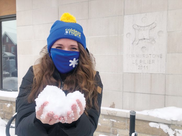 Amber Bramber stands in front of Cornerstone's beige and brick building holding snow in her bare hands while wearing a blue mask and matching toque|Two Cornerstone staff stand in front of the beige and brick building wearing blue masks and toques and toss snow in the air