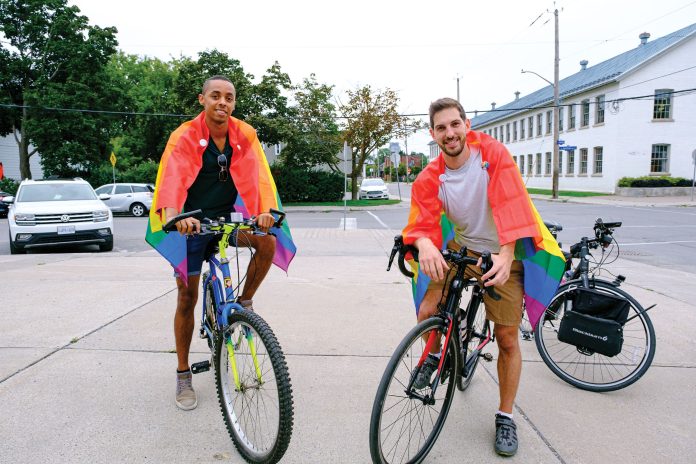 Two men sit on bikes and wear rainbow Pride flags as capes.||A group of cyclists go along a route near Parkdale Park wearing rainbow attire.|A corgi wearing a rainbow lei sits in a bike basket.