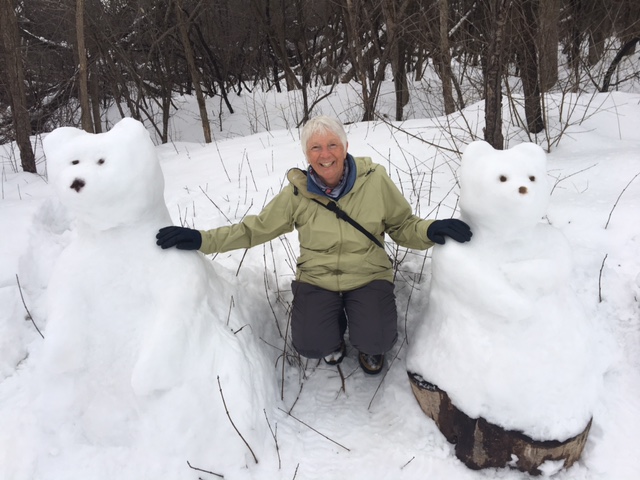 A woman wearing a green snow jacket and grey snow pants sits between two bears made of snow in Ottawa||||