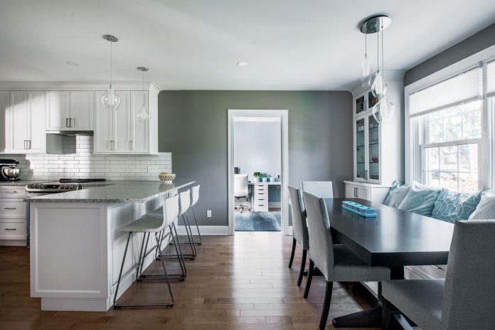 A renovated kitchen and dining room is seen in a staged home photo in a Westboro house|A desk with two stations is seen in a renovated home.|A picture of the kitchen pre-renovation with 1940s style|A renovated dining room is seen with white cabinets and a black table with white chairs|A renovated kitchen in a Westboro home is seen. It has a dark wood floor and white kitchen cabinets and chairs.