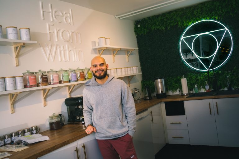 A man stands in Pure Apothecary on Wellington West Street. There are coffee and tea packages on the wall on the left and a green