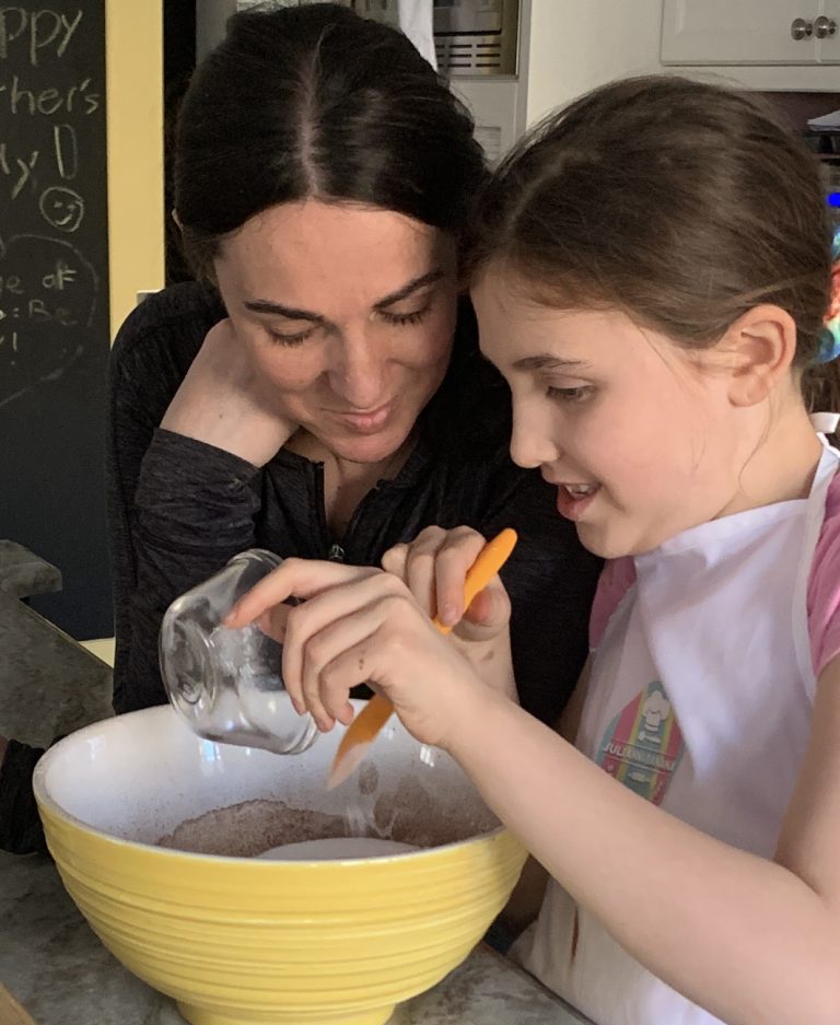 A mom and daughter pour baking mix into a yellow bowl.||