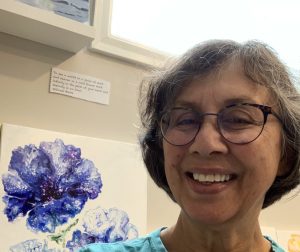 A headshot of Manju Sah with a painting of a purple flower behind her