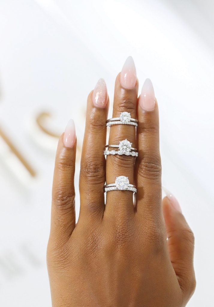 A hand wears three moissanite rings on its middle finger against a white background