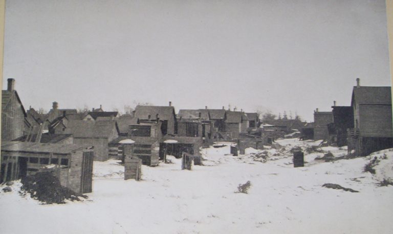 A black and white picture from 1911 of outhouses behind houses on a snowy day in Hintonburg.||