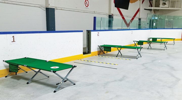 Green cots are set up six feet apart on the floor of the Tom Brown Arena Respite Centre