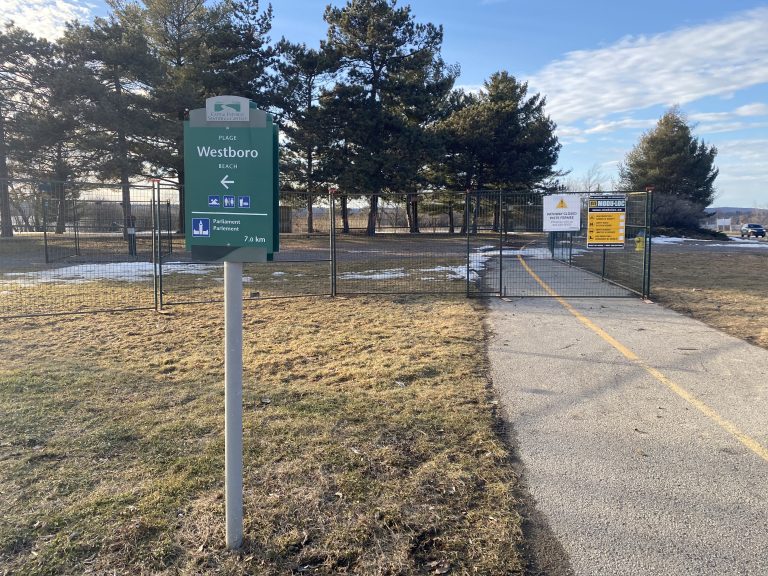 The path next to Westboro Beach on a sunny day. There is a green sign for the beach in the front.|Westboro Beach with a cloudy sunset in the background. The beach is covered with a small layer of snow.|A close up of a white "no admittance" sign at Westboro Beach with a road and snow in the background.