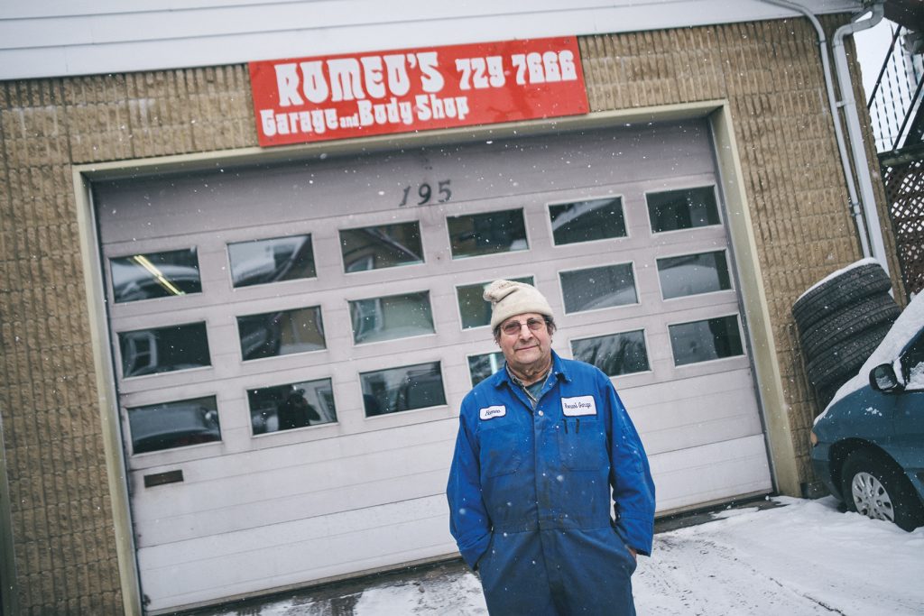 A man stands outside of Romeo's Garage & Body Shop's front garage door in the snow