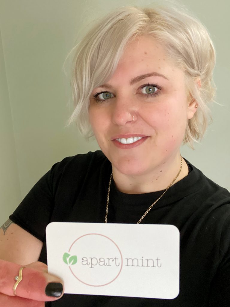 A woman holds up a business card that says "ApartMint" on it.