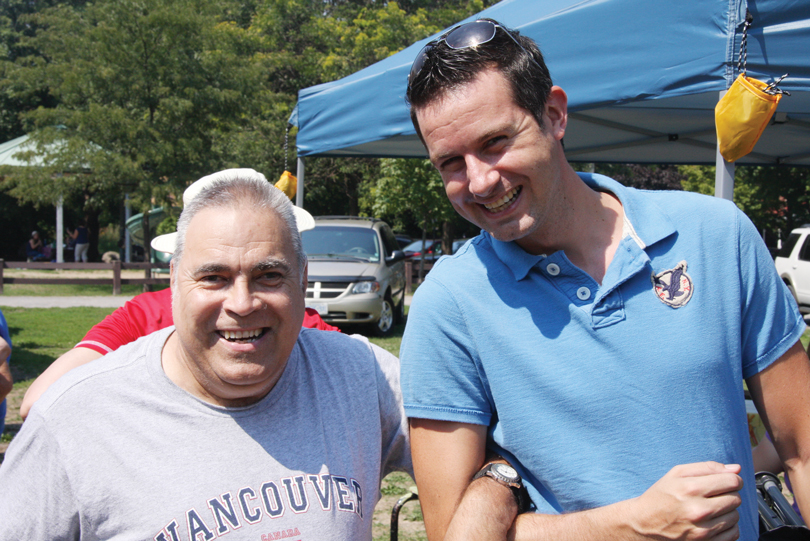 Two men have their arms linked at an outdoor ABLE2 event on a sunny day in Ottawa.