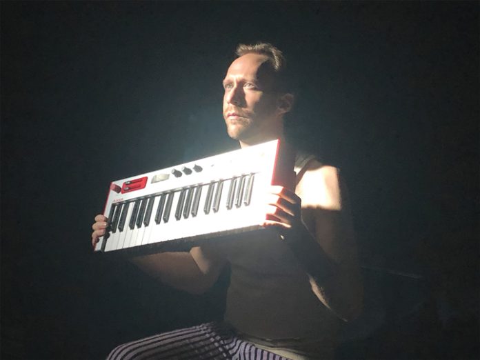 Scottie Irving sits on a dark stage and holds up a keyboard in the lights