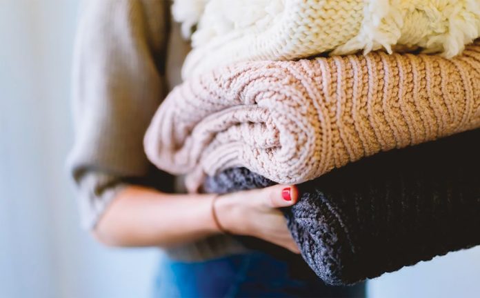 A stock image of a woman carrying a pile of sweaters