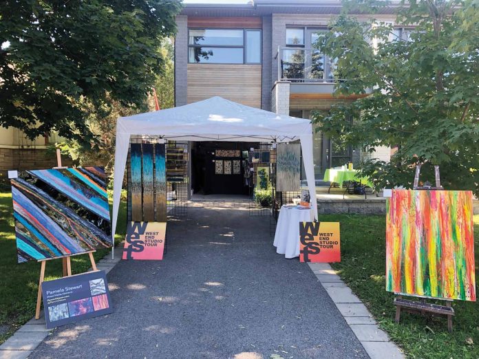 A white tent outdoors is surrounded by different art works. It is a sunny day.