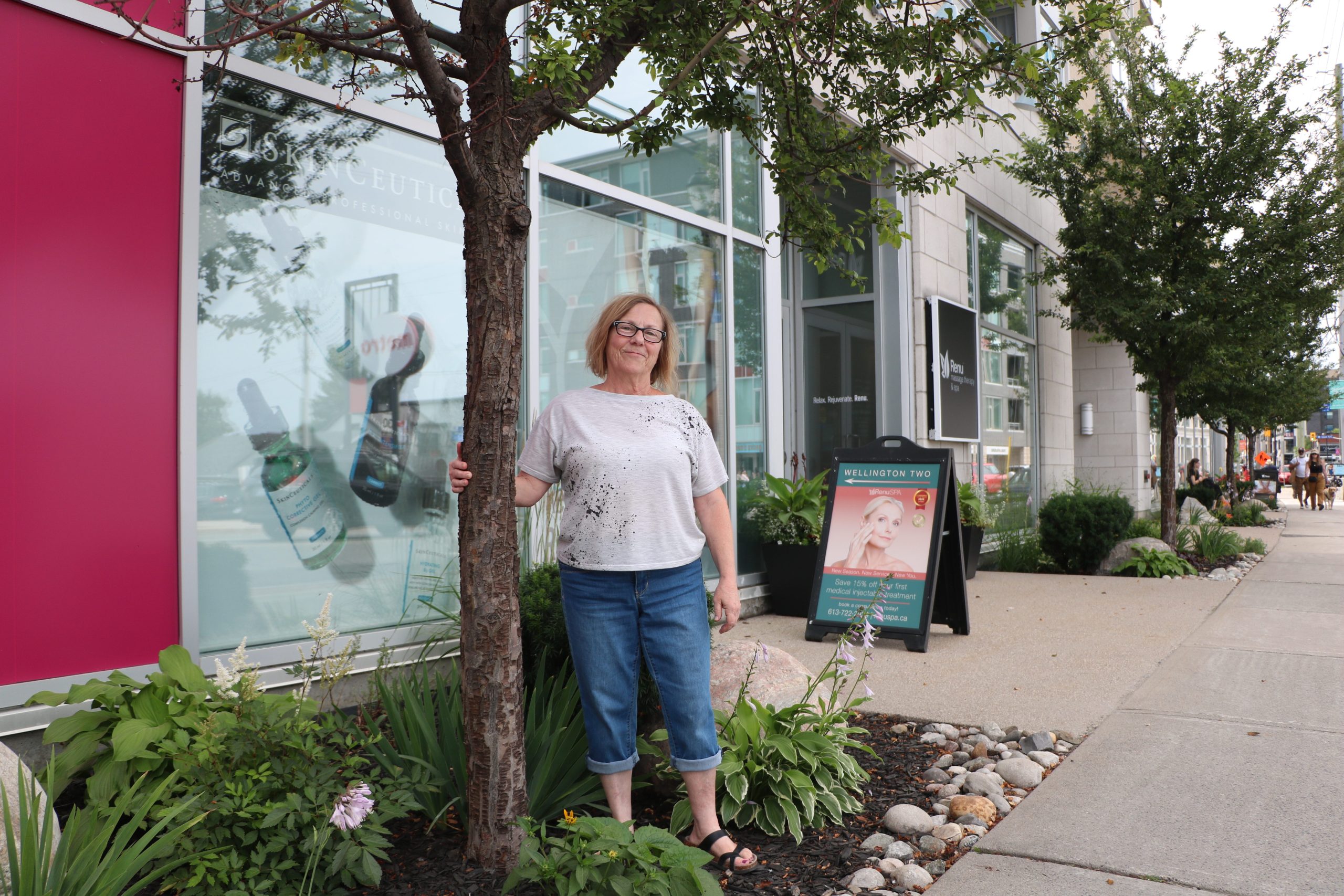 Carolyn holds onto a tree and poses for a photograph outside her building 