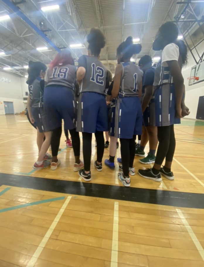 A group of female junior high students stand together on a basketball court.|