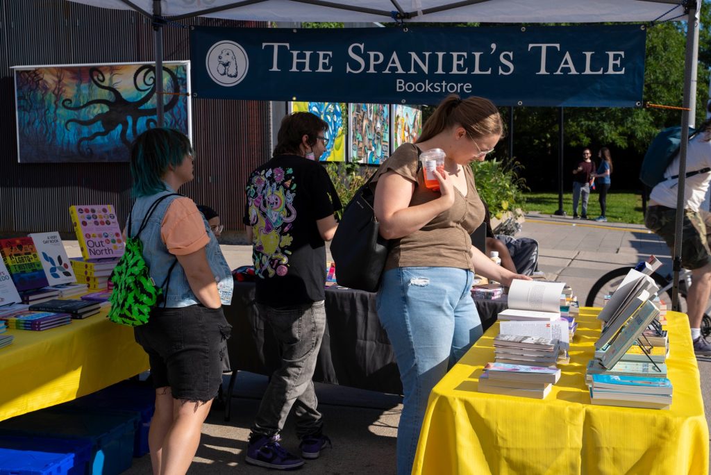 Three people look at a table for the Spaniel’s Tale bookstore. 