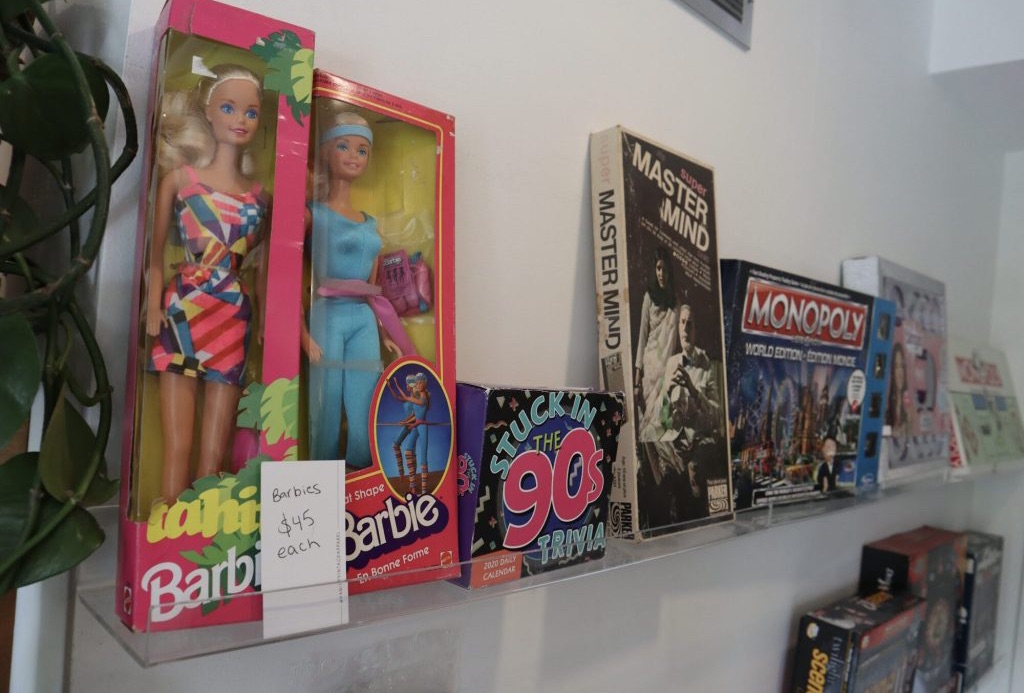 Two Barbie food and other toys from the 90’s sit on a shelf. 