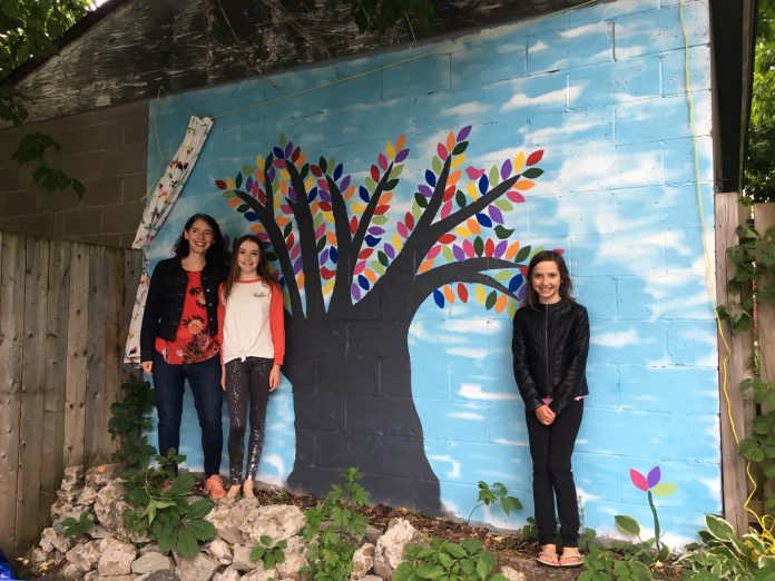 A photo of the Thomson family and their painted tree mural in Hintonburg.|A photo of the colourful tree mural painted by the Thomson family in Hintonburg during the pandemic.