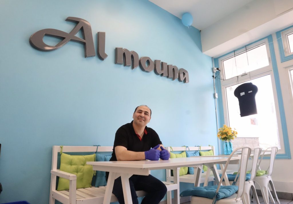 Mohamed sits inside the restaurant. The walls behind him are blue. 